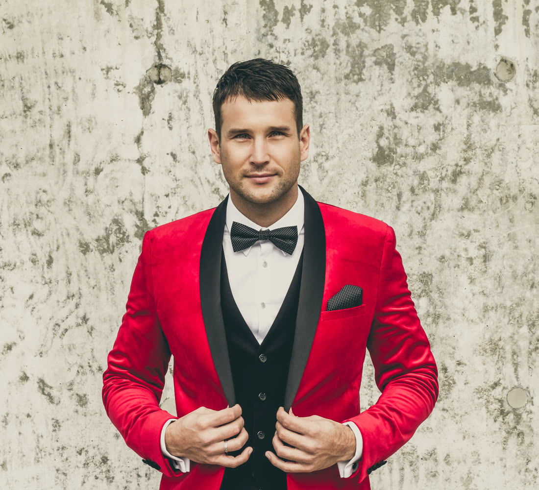 Sam Ludeman in a red velvet tuxedo jacket and bow tie, looking straight at the camera
