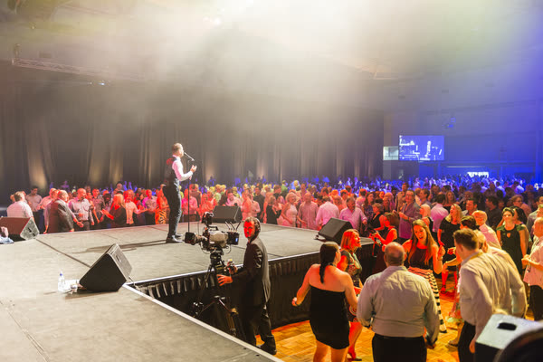 Sam singing at the edge of the stage, seen from behind, with a packed dance floor of guests in front of him