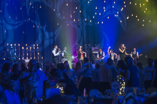 The full line-up with singers, dancers and guitars under hanging lights, guests up and dancing in front